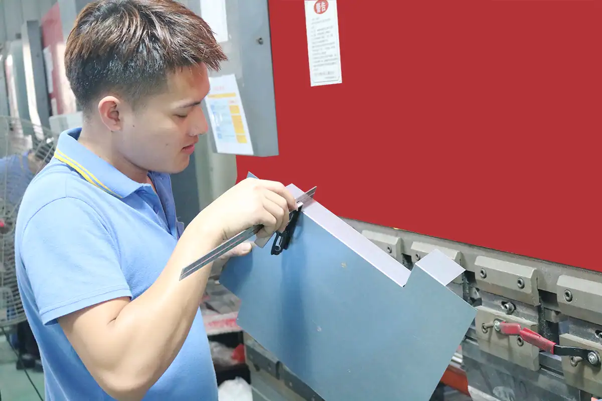 Worker forming stainless steel sheet metal on a bending press at the FLAMEMAX factory in Foshan